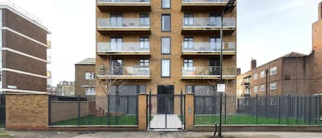 Un immeuble résidentiel à plusieurs étages, doté de balcons, d’une entrée sécurisée et d’une allée pavée.