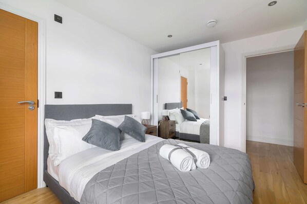 A bedroom with a bed, a bedside table, a nightstand, a mirror, and a door.