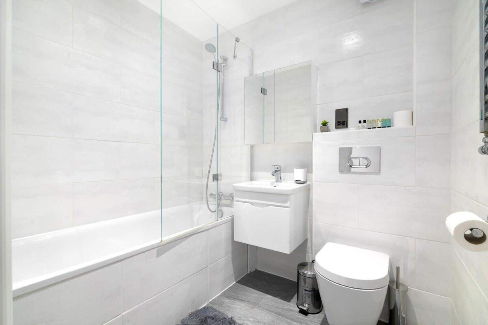Et moderne badeværelse med en glasvæg omkring brusenichen, en hvid vask og et toilet.