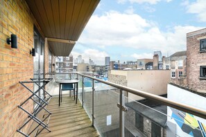 Un balcon avec une table et des chaises, donnant sur un paysage urbain composé de différents bâtiments.