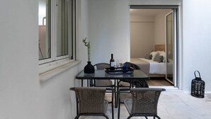 Habitació petita i moderna amb un llit, una taula amb un ram i vi, i cadires de vimet.