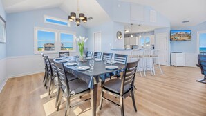 Een eetruimte met een tafel voor zes personen, een kroonluchter en uitzicht op het strand door grote ramen.