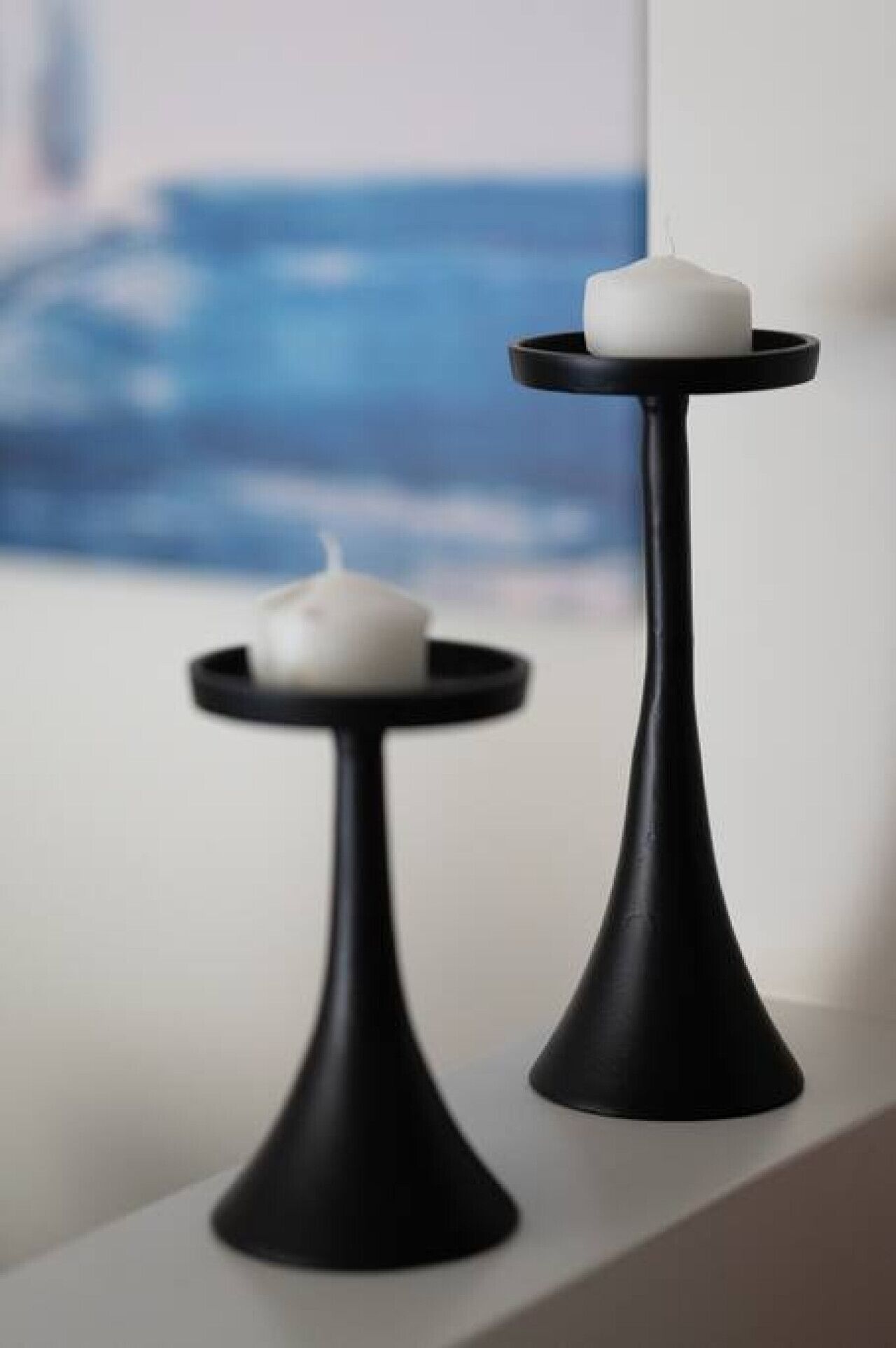 Two black candle holders with white candles on a white surface.
