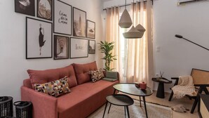 Una sala de estar con un sofá rojo, una mesita redonda y una silla. Hay cuadros enmarcados en la pared y una planta en maceta.
