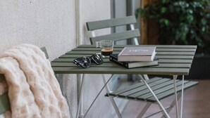 Una mesa metálica verde con un libro, una taza de café y unas gafas de sol.