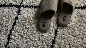 Slippers op een kamerbreed tapijt naast een bed met een donkere deken.