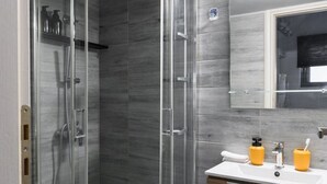 Een moderne badkamer met een glazen douchecabine, een wit toilet, een houten wastafelmeubel met spiegel en een betegelde vloer.