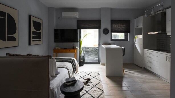 Een moderne woonkamer met een bank, een salontafel en een televisie. Er is een keukenhoek met kastjes en een aanrecht.