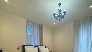 A neatly made bed with white linens, a bedside table with a lamp, and a chandelier above. - Residence VillaBelleFleur-Apartment La Gentiane (Château-Ville-Vieille)