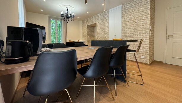 A modern dining area with a long wooden table, black chairs, and a chandelier. - Residence VillaBelleFleur-Apartment La Gentiane (Château-Ville-Vieille)