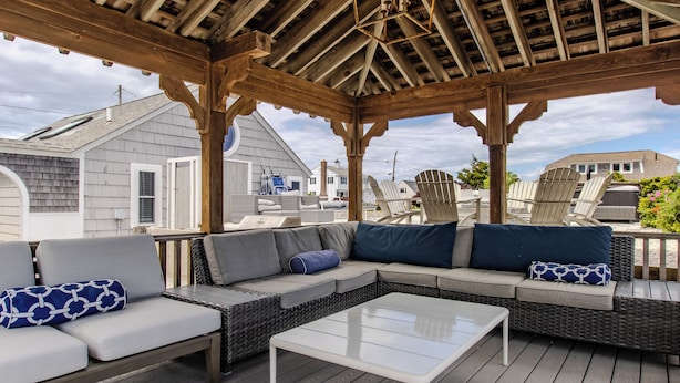 An outdoor covered patio with a wooden ceiling, wicker furniture, and a view of neighboring houses.