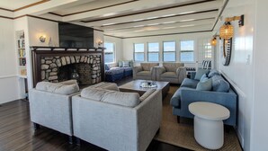 A spacious living room with a stone fireplace, multiple seating areas, and large windows overlooking a body of water.