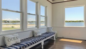 A room with large windows, a bench with striped cushions, and a view of a beach and water.