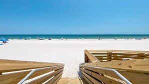 A wooden boardwalk leading to a beach with umbrellas and people.