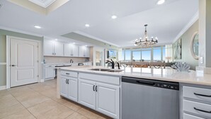 A spacious kitchen with white cabinetry, a large island with a sink, and a modern chandelier.
