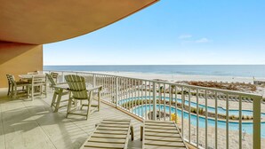 A balcony with a view of the beach, a pool, and outdoor seating.