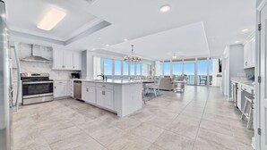 A spacious kitchen with a central island, modern appliances, and large windows offering views of the outdoors. - Newest Beachfront Complex!!  Professionally Decorated 4BR!!  Lazy River!! (Orange Beach)