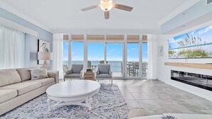 A spacious living room with a large window overlooking the ocean, a ceiling fan, and a fireplace. - Newest Beachfront Complex!!  Professionally Decorated 4BR!!  Lazy River!! (Orange Beach)