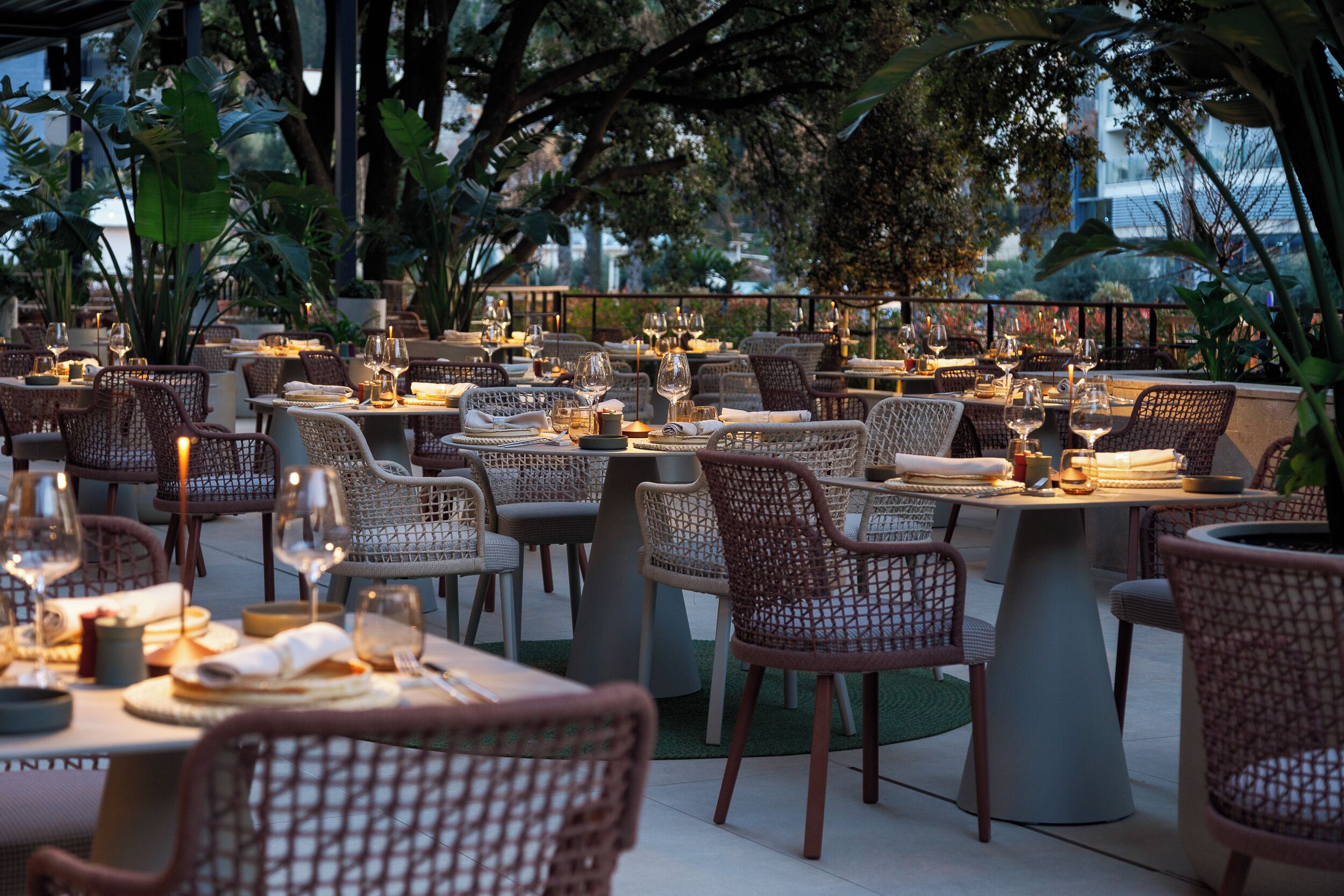 An outdoor dining area with wicker chairs and tables, surrounded by greenery.