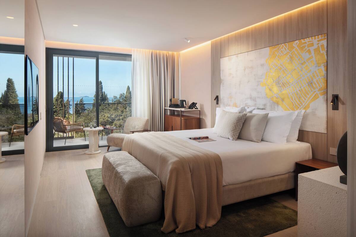 A modern hotel room with a large bed, a desk, a chair, and a view of the outdoors.