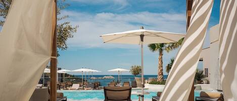 A poolside area with lounge chairs, umbrellas, and a view of the sea.