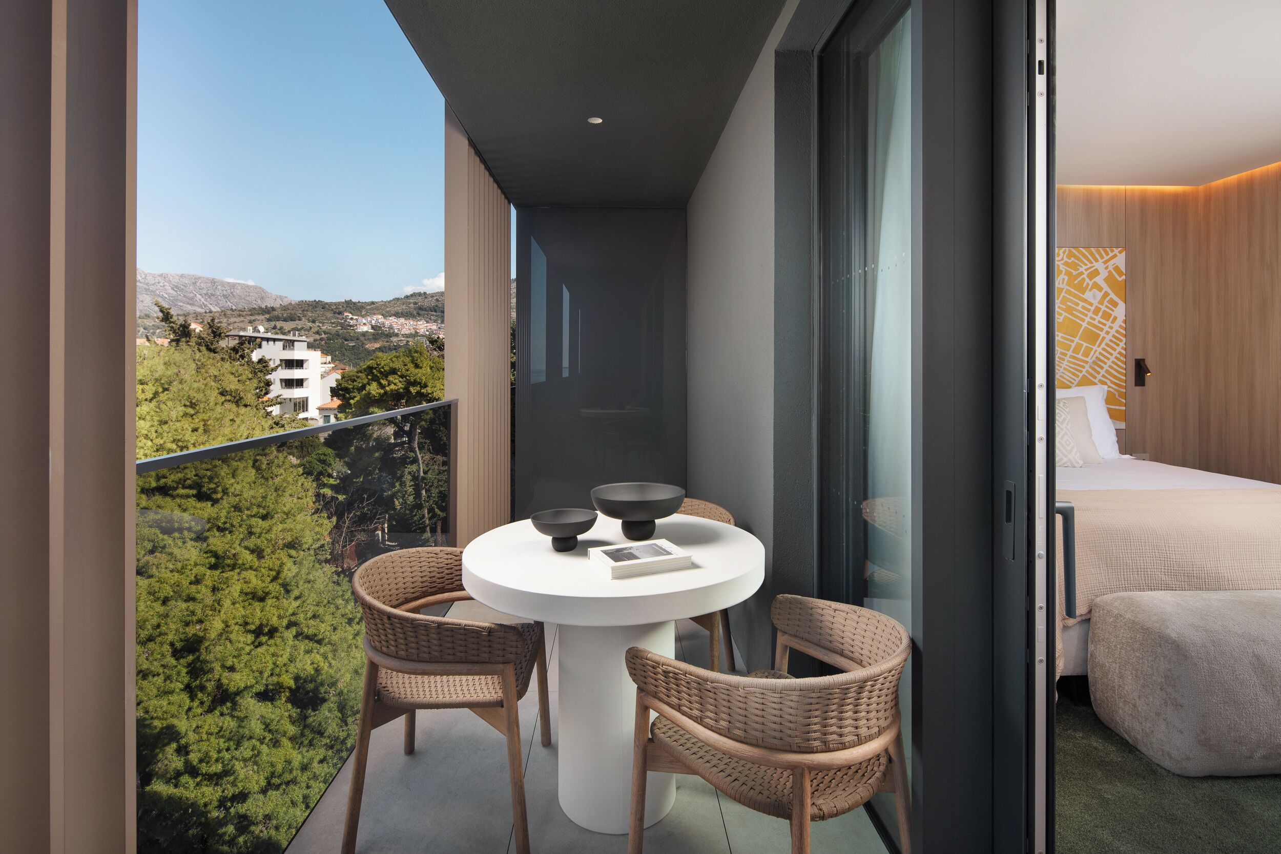 A balcony with wicker chairs, a round table, and a view of a mountainous landscape.