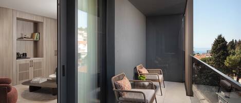 A balcony with two wicker chairs and a coffee table, a sliding glass door leading to a kitchen area, and a view of the cityscape.