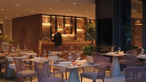 An outdoor dining area with tables and wicker chairs, a bar with bottles, and a view of the city at dusk. - Hotel Sumratin (Dubrovnik)