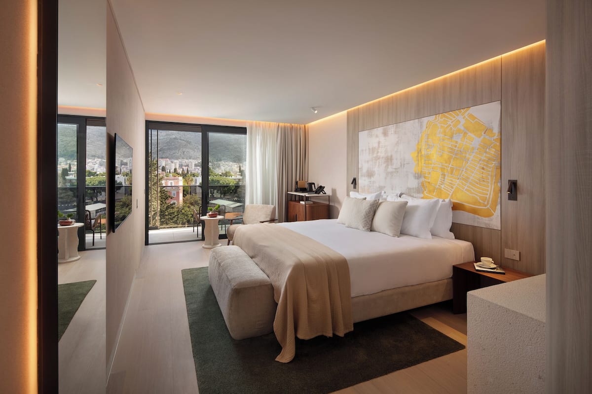 A modern hotel room with a large bed, a map artwork, a balcony with a view, and a desk with a chair.