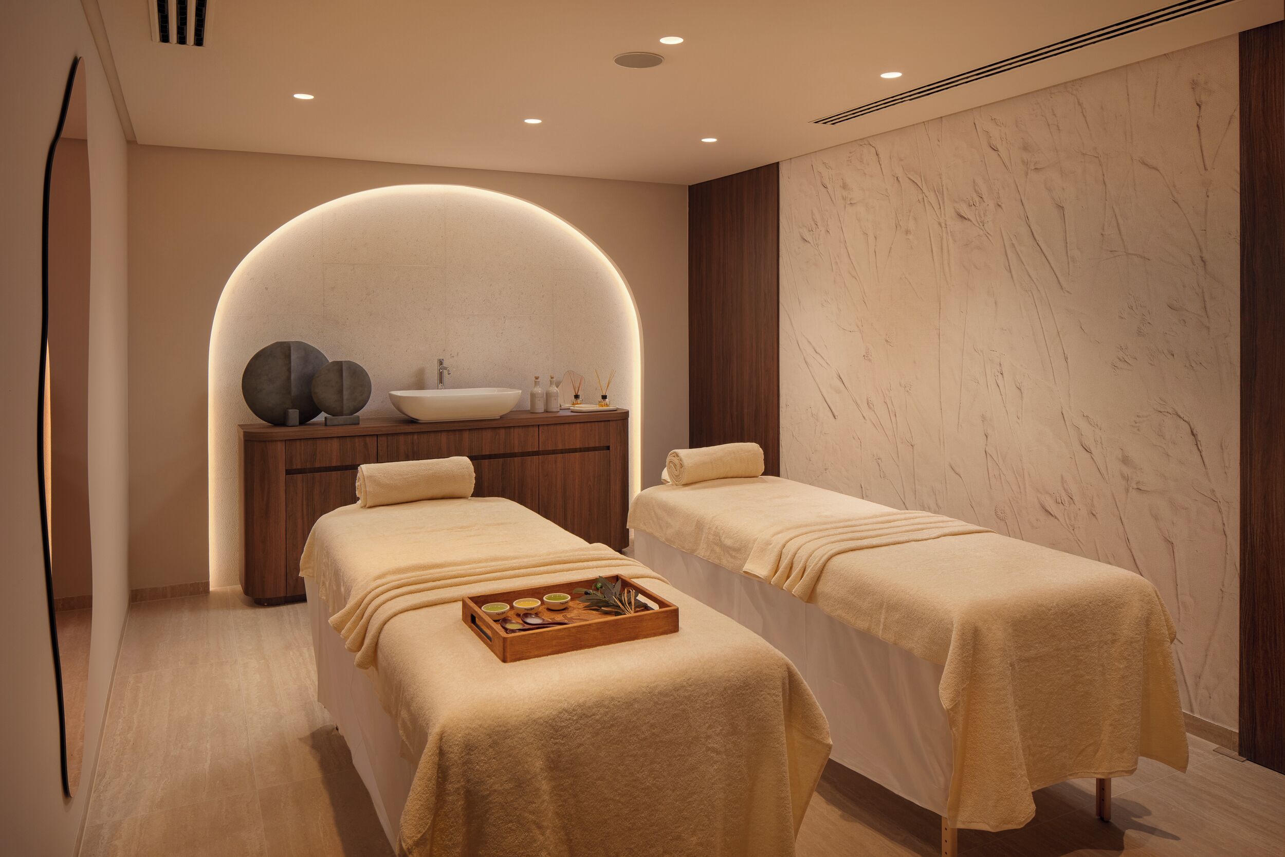 A spa room with two beds, a wooden cabinet, a sink, and a tray with amenities.
