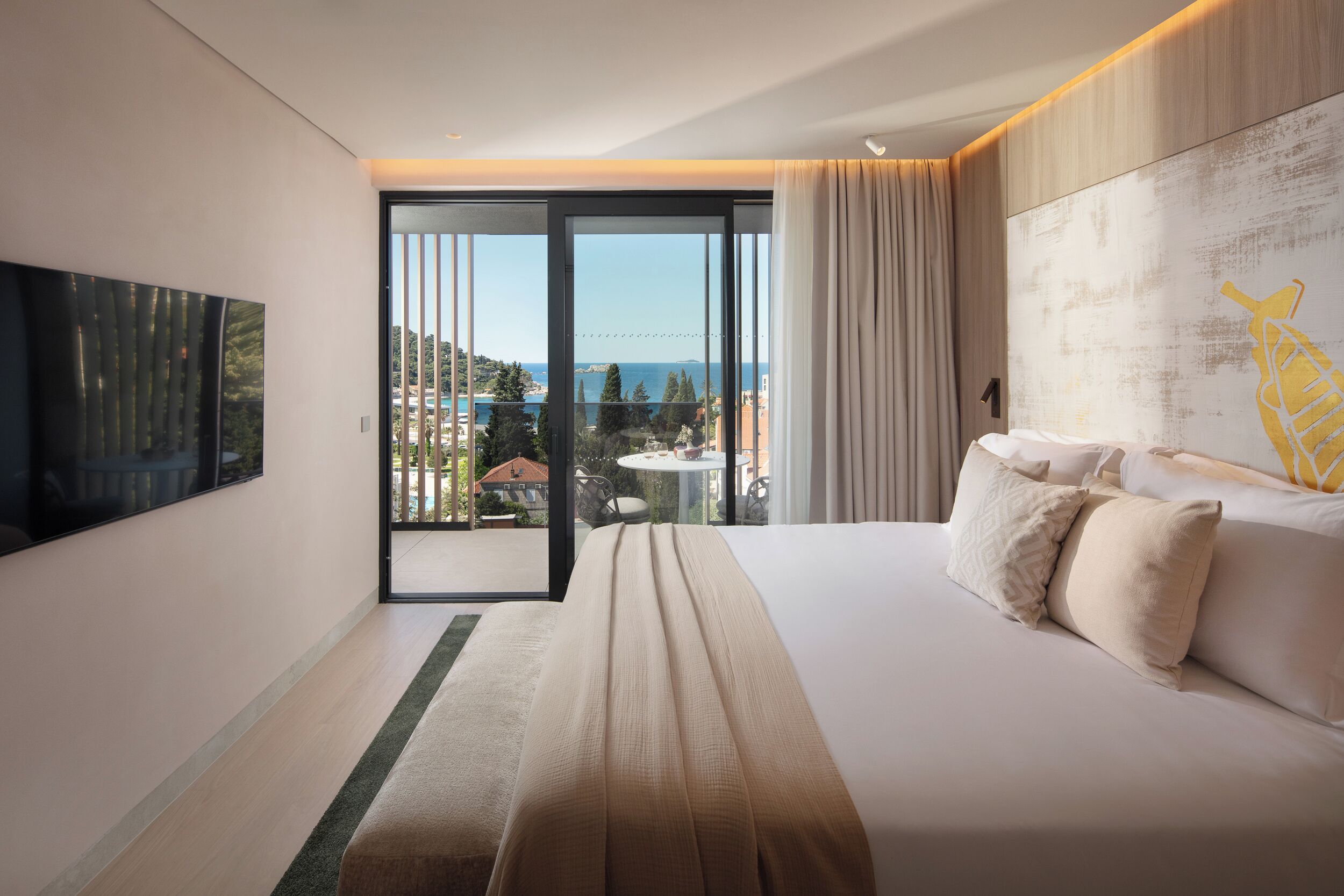 Et moderne hotelværelse med en stor seng, et fladskærms-TV, en balkon med havudsigt og et spiseområde.