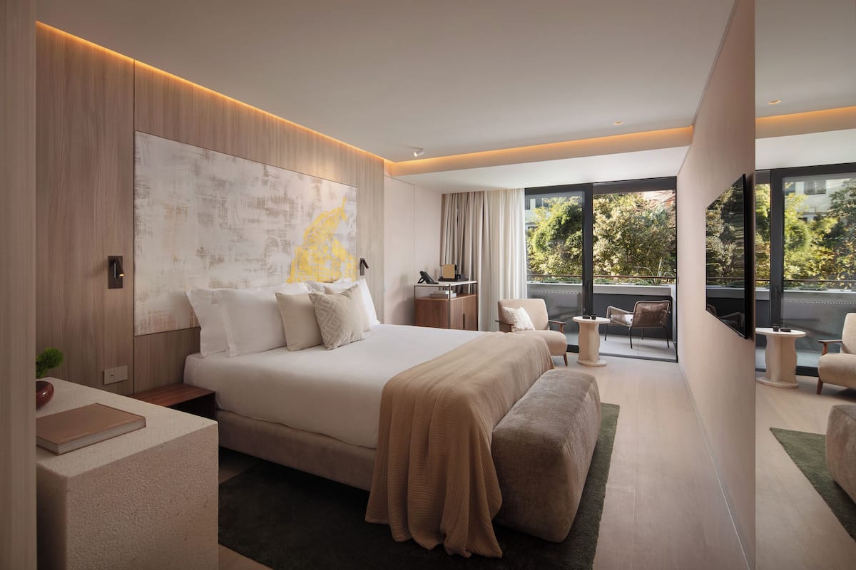 A modern hotel room with a large bed, a view of the outdoors, a desk, and a chair.