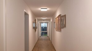A hallway with wooden flooring, white walls, and framed artwork on the walls. - Modern cozy purple apartment (Bielefeld)