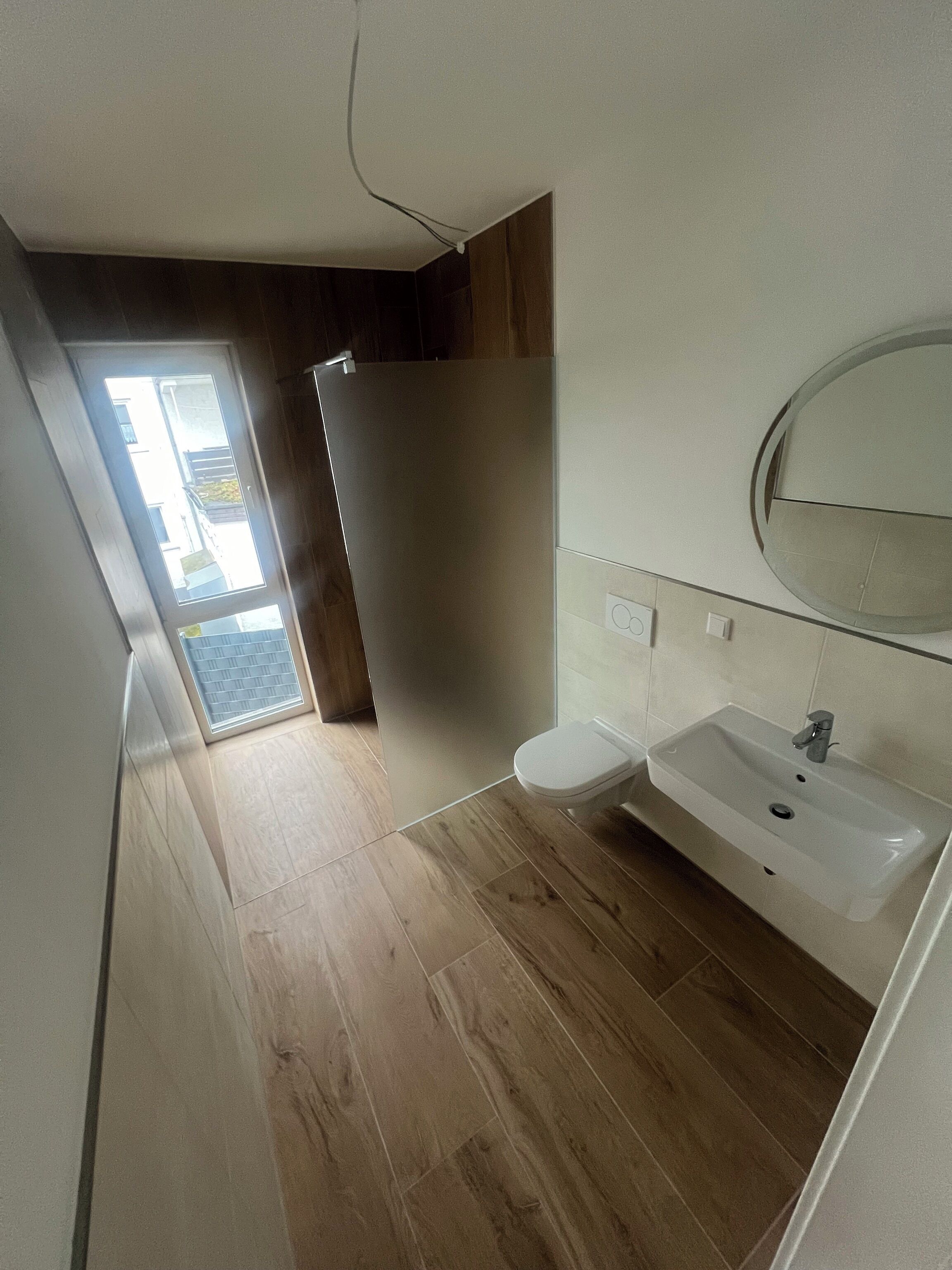 A modern bathroom with a wooden floor, a white sink, and a mirror above it.