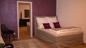A bedroom with a bed, a chair, and a small table. - Modern cozy purple apartment (Bielefeld)