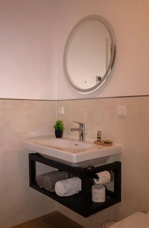 A bathroom with a white sink, a mirror, a small potted plant, and a shelf with towels and toilet paper. - Modern cozy purple apartment (Bielefeld)