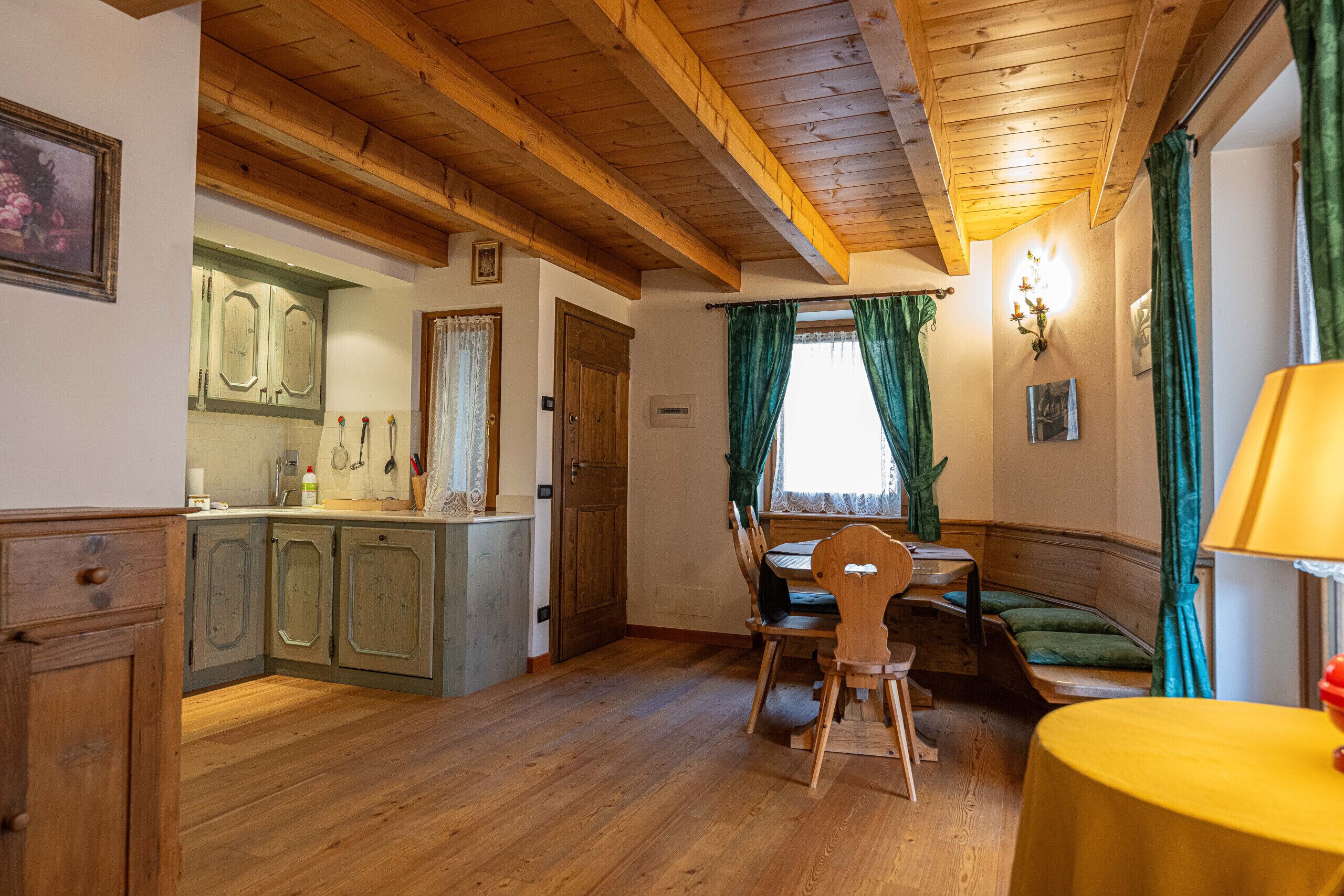A wooden-floored room with a dining table, chairs, a bench, and a small table with a lamp.