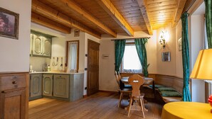 Ein Zimmer mit Holzboden, einem Esstisch, Stühlen, einer Bank und einem kleinen Tisch mit Lampe.