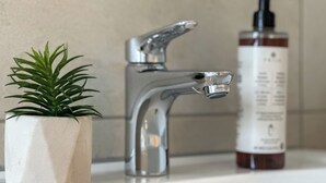 Un lavabo de salle de bain avec un robinet moderne, une plante en pot et un flacon de savon liquide.