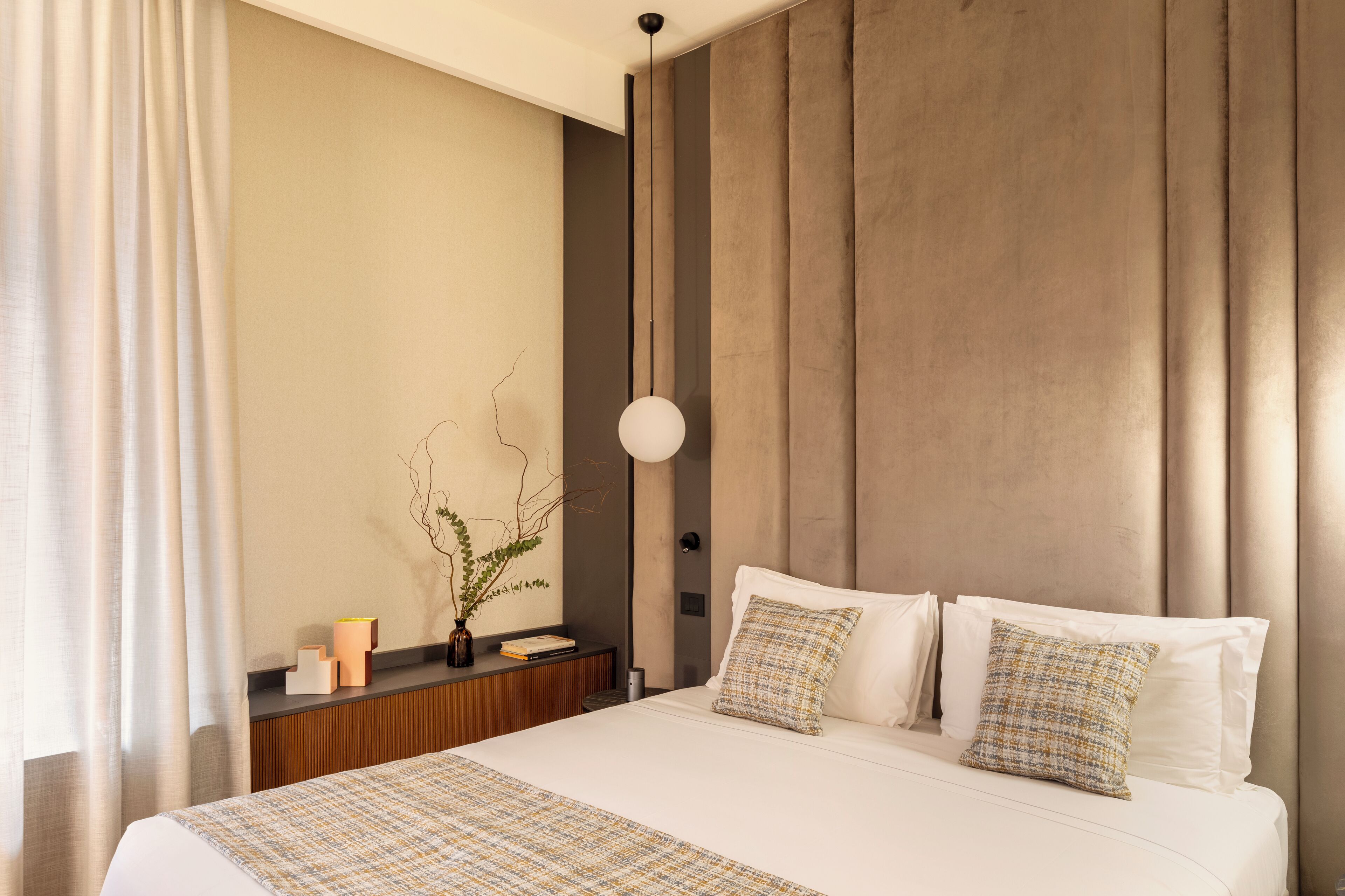 Ein modernes Hotelzimmer mit einem großen Bett, einem Nachttisch, einer Wandlampe und einer Zimmerpflanze.