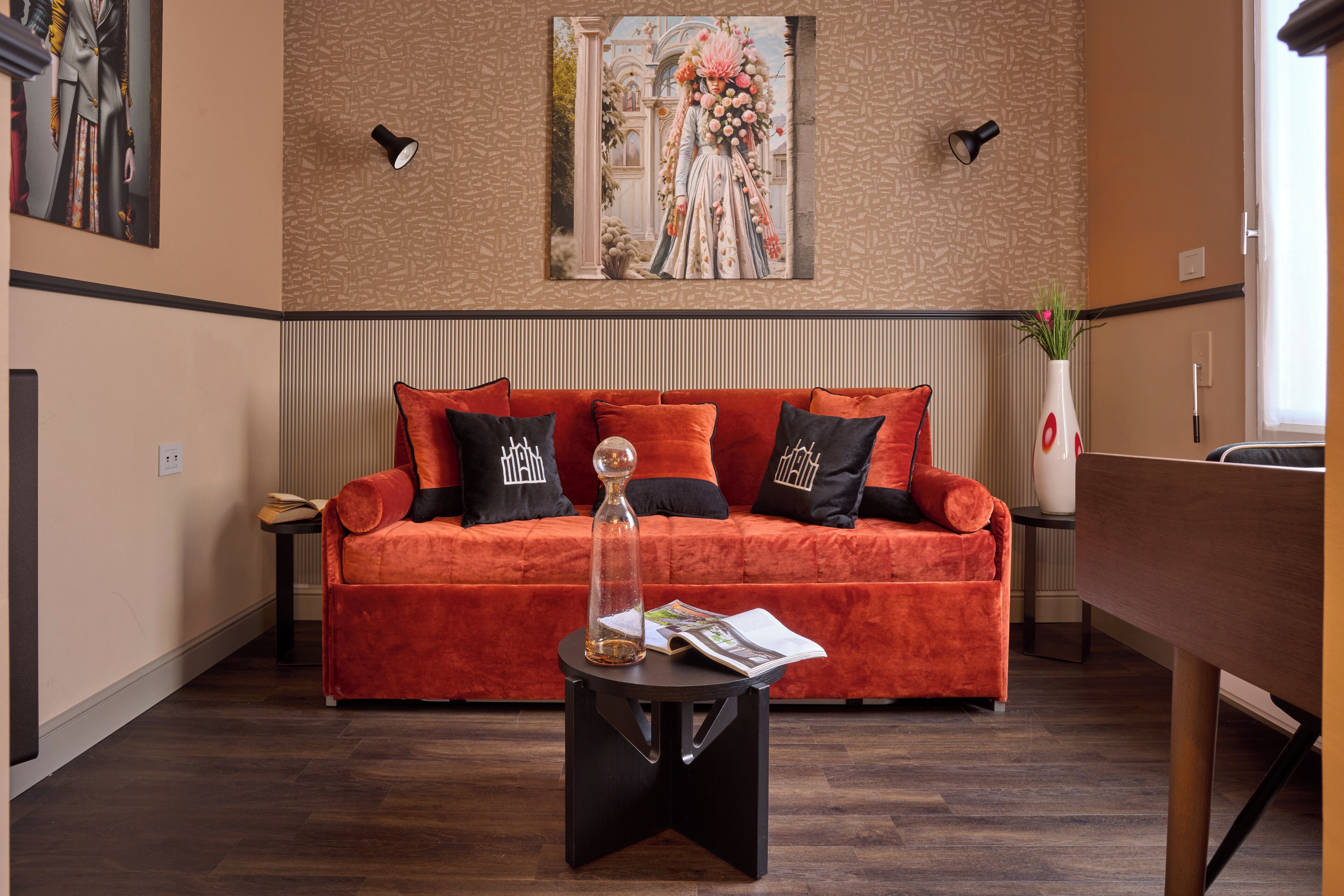 Ein Wohnzimmer mit einem roten Sofa, schwarz-weißen Kissen, einem kleinen schwarzen Beistelltisch und einem Glastisch mit einem Buch und einer Vase.