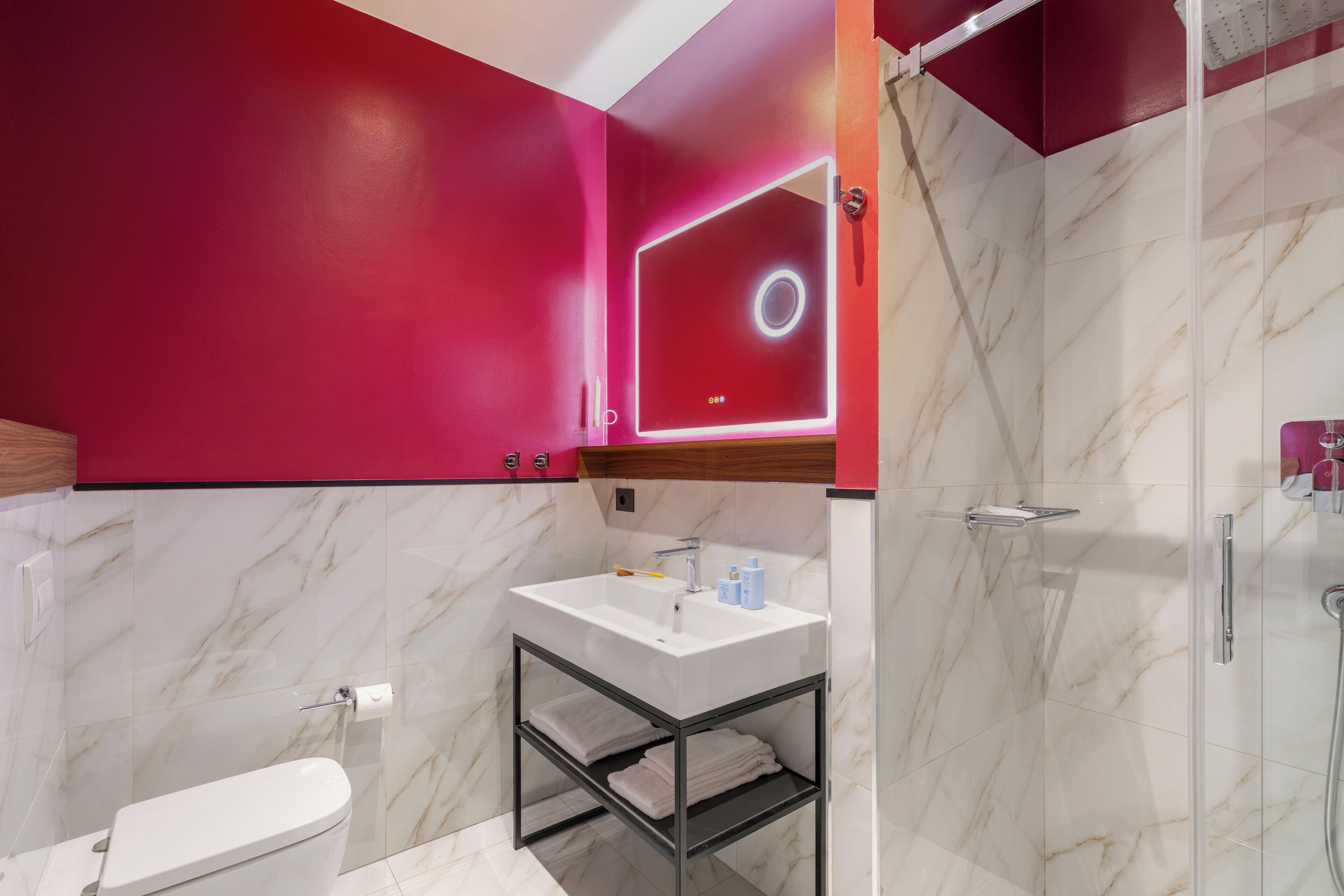 A modern bathroom with a white sink, a mirror with a circular light, and a shower area.