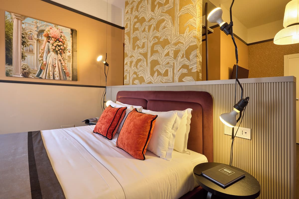 Una habitación de hotel con una cama grande, una mesita de noche, una lámpara, un cuadro en la pared y un papel tapiz estampado.