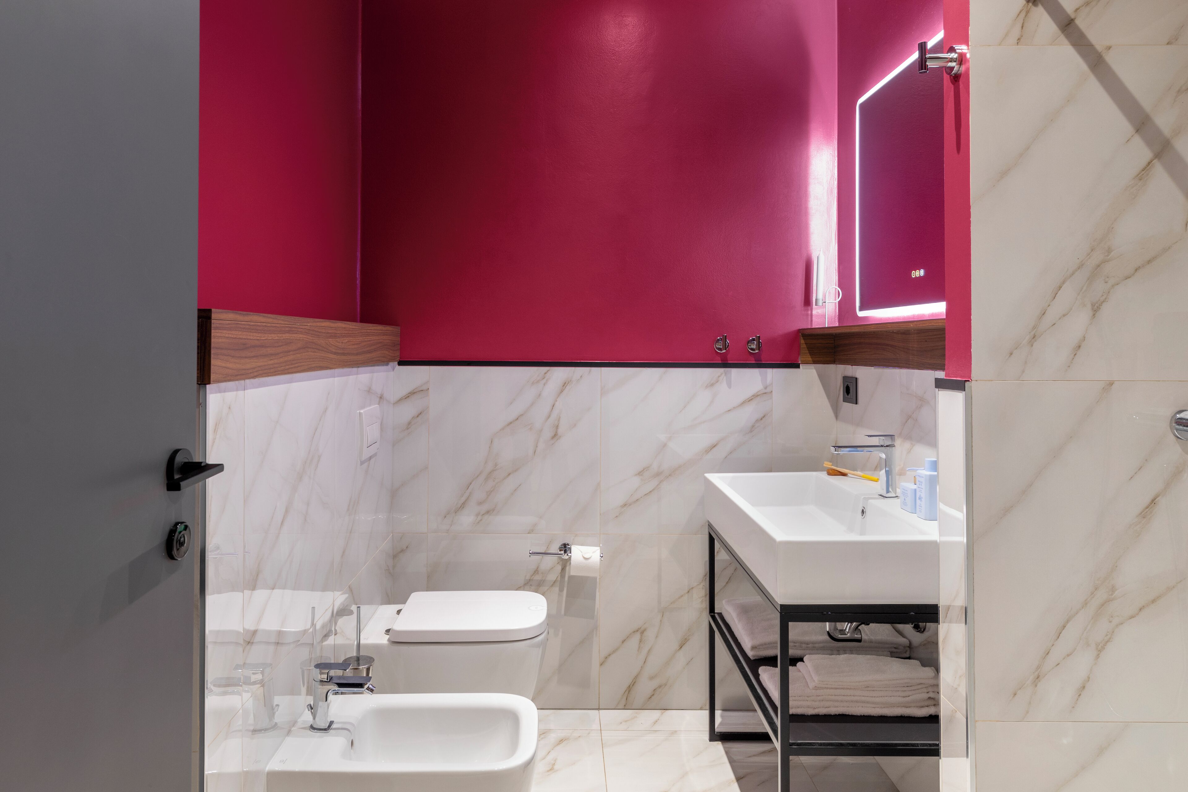 Ein modernes Badezimmer mit Toilette, Bidet und Waschbecken, mit Marmorfliesen und einer rosafarbenen Akzentwand.