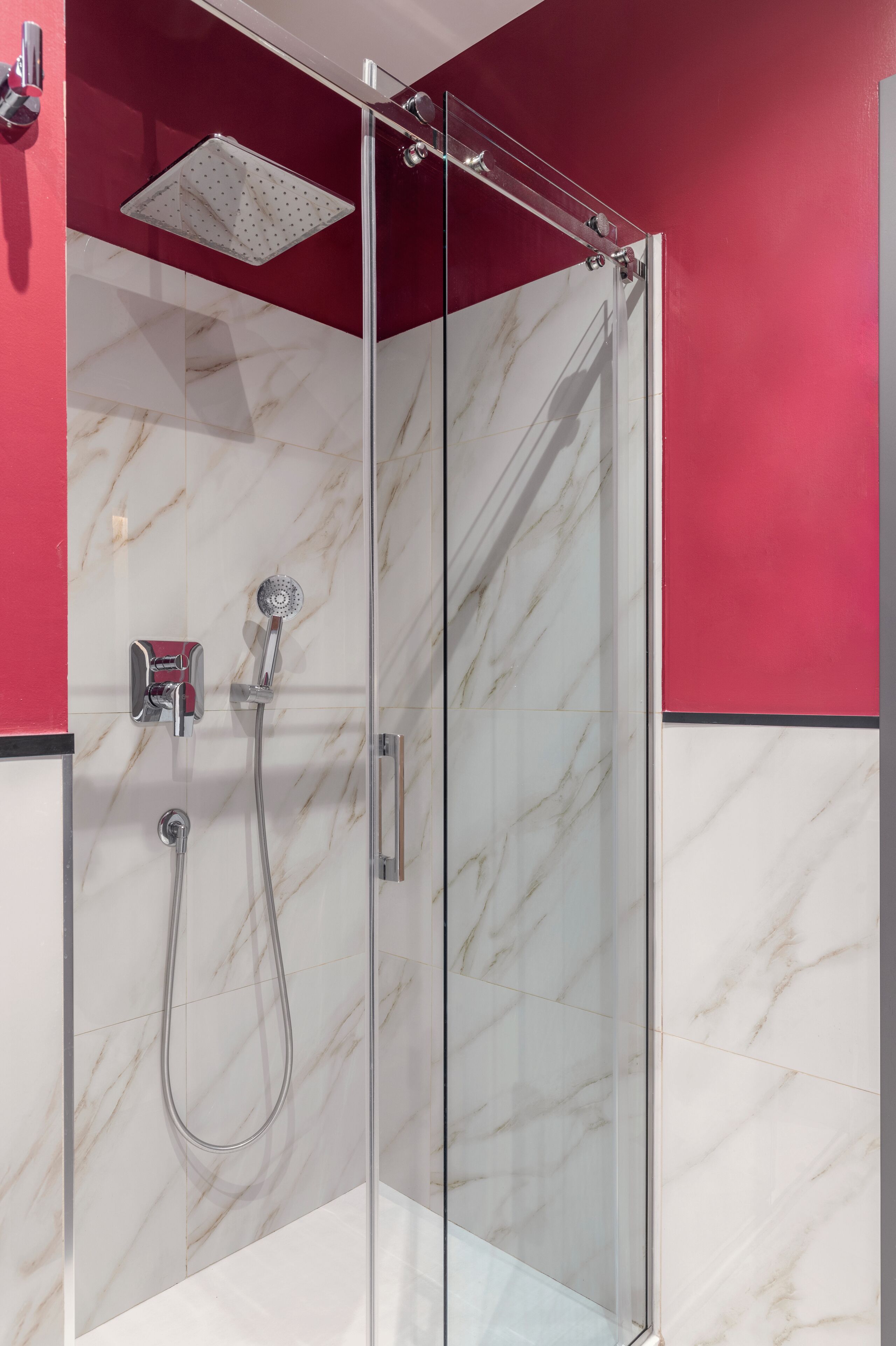 Ducha con cerramiento de vidrio, cabezal de ducha de mano y panel de control en la pared.