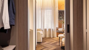 A hotel room with a wooden herringbone floor, a white sofa, a small table with a vase, and a large window with sheer curtains. - LUMERA STAY - Brera (Milan)
