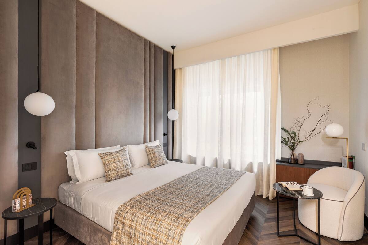 Una habitación de hotel moderna con una cama grande, una mesita redonda, una silla y un escritorio con una lámpara.