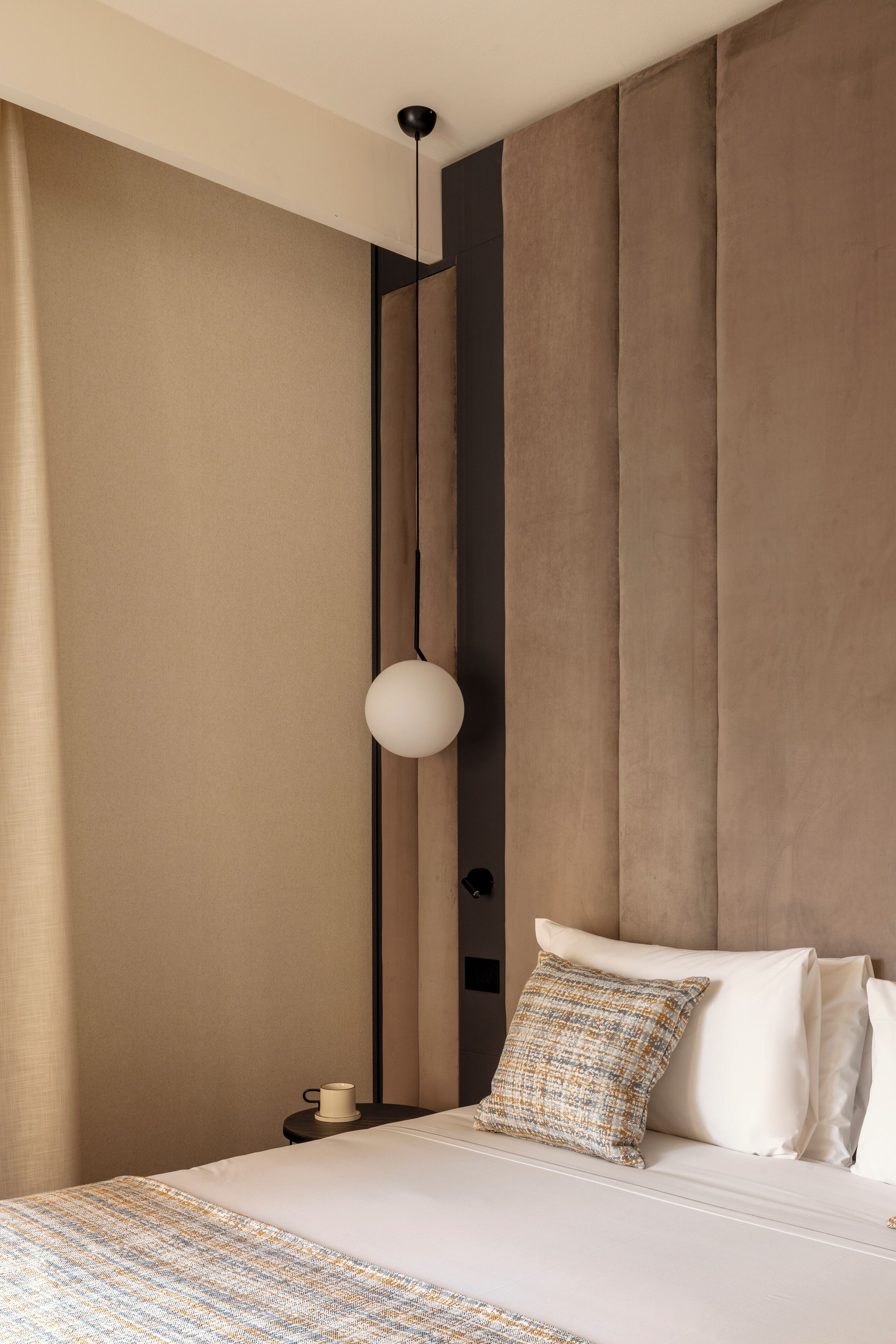 A modern hotel room with a large bed, a bedside table with a lamp, and a large window with curtains.
