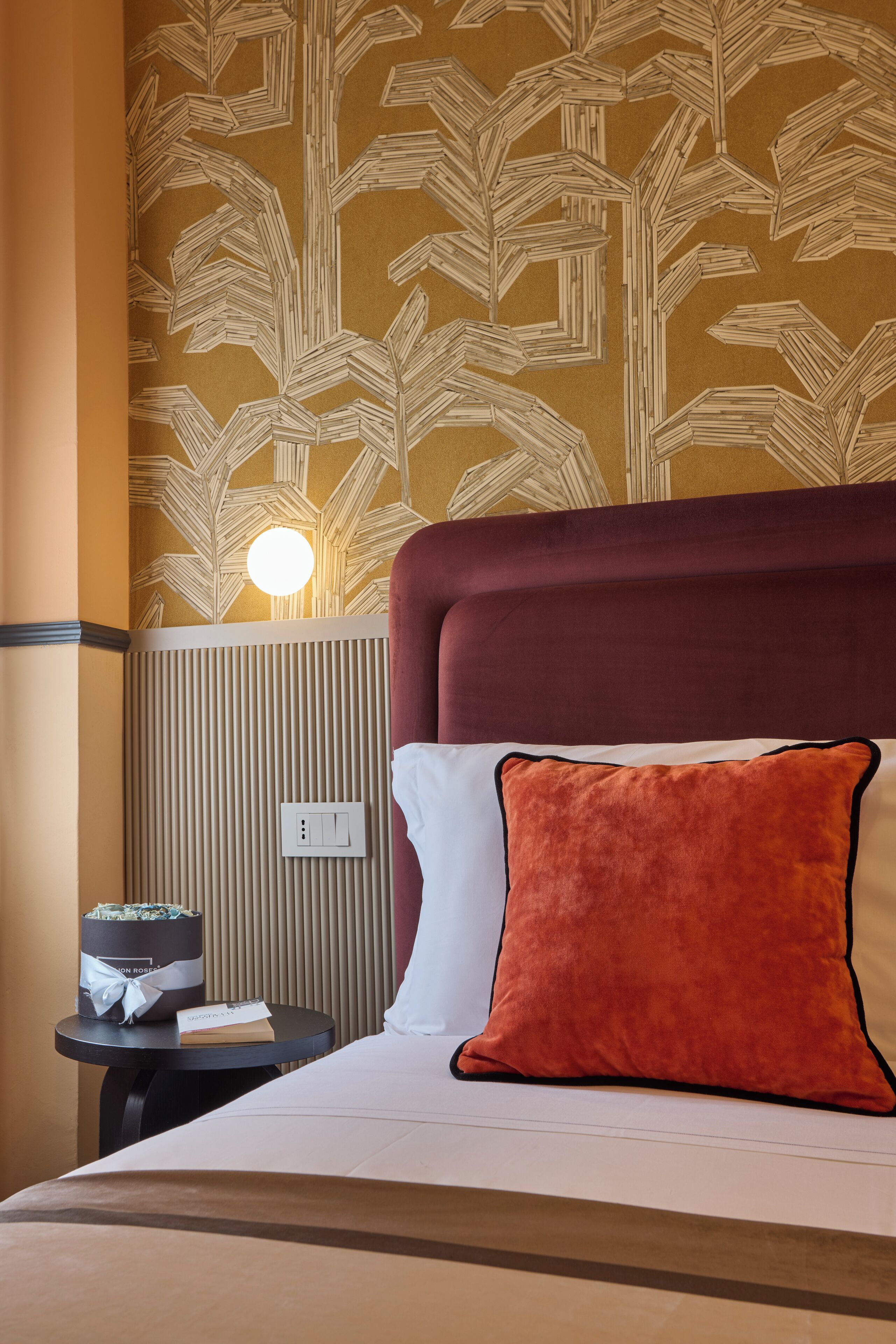 A hotel room with a bed, a nightstand, a lamp, and a wall with a leaf pattern.