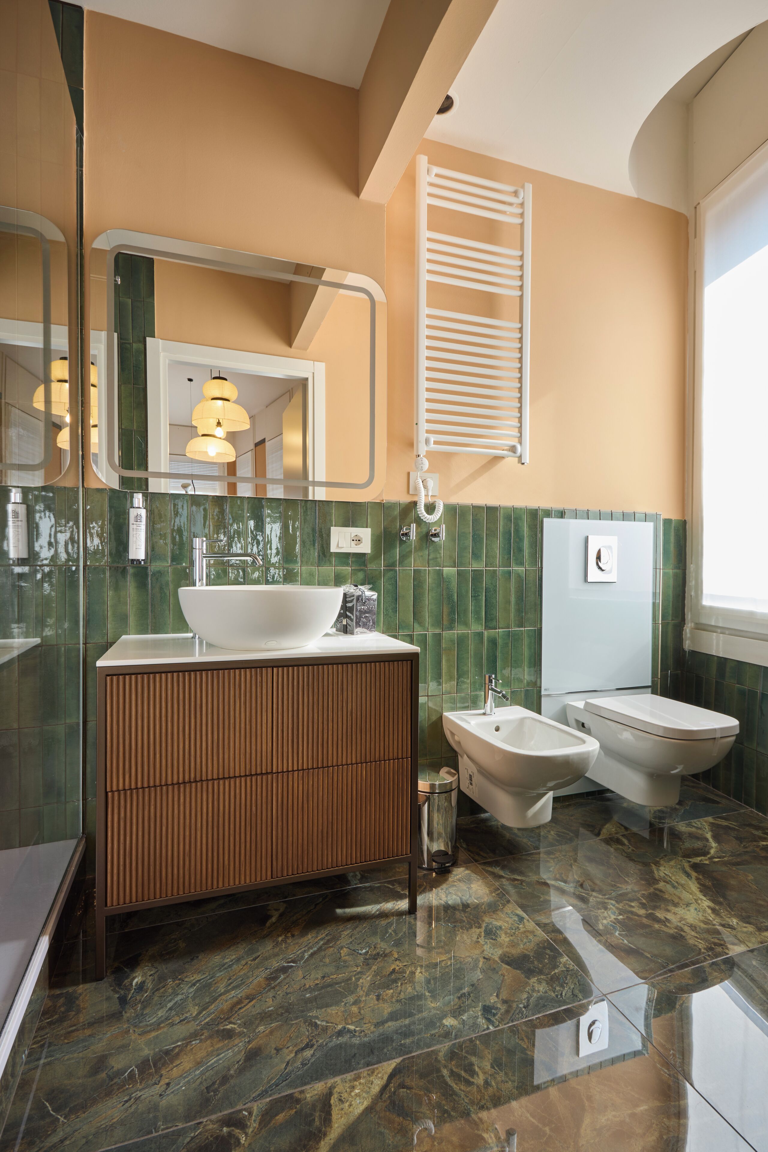A modern bathroom with a large sink, bidet, and bathtub, featuring green tiled walls and a marble floor.